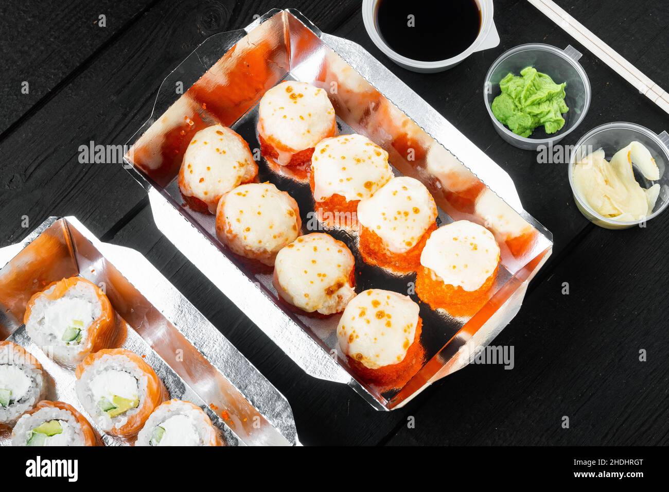 Sushi-Brötchen zum Mitnehmen in Behältern, philadelphia-Brötchen und gebackene Garnelenrollen auf schwarzem Holztisch im Hintergrund Stockfoto