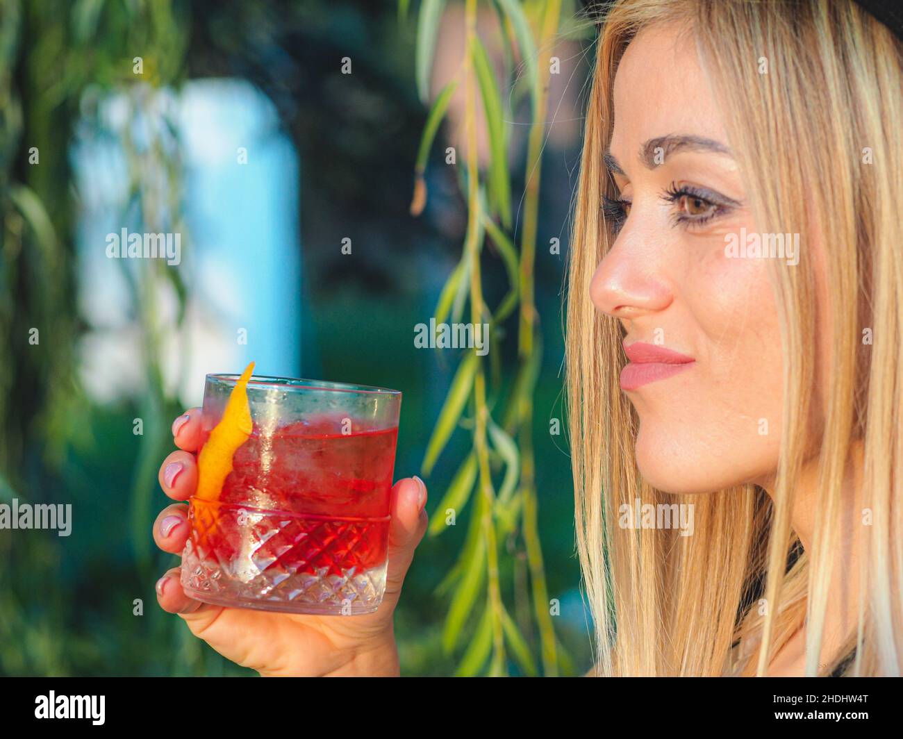 Selektiver Fokus einer Italienerin, die unter dem Baum steht und einen erfrischenden Cocktail in der Hand hält Stockfoto