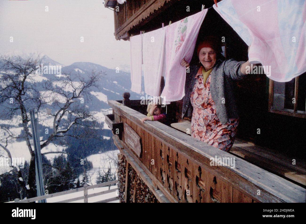 Ältere Dame, die ihre Wäsche online waschen lässt. Reife Frau hängt die Wäsche vor ihrem Haus in den alpen an der Linie. Frau schaut durch die Kleidung Stockfoto
