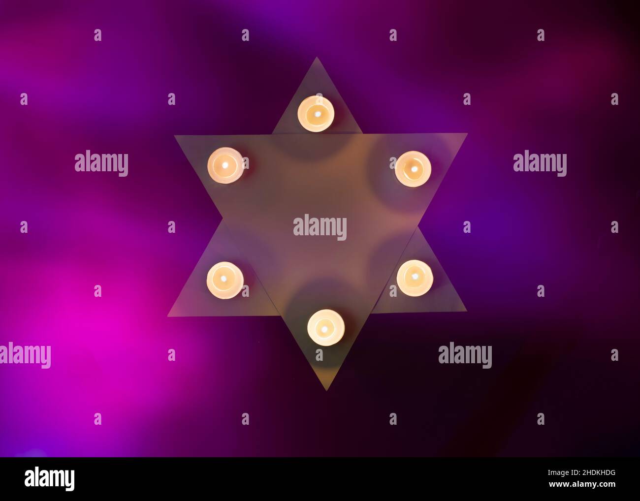 Davidstern, geschmückt mit brennenden Kerzen auf violettem Flammenhintergrund. Holocaust-Gedenktag. Stockfoto