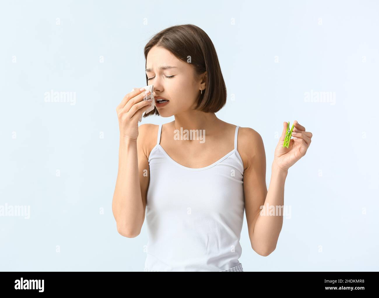 Kranke junge Frau mit Wäscheklammer auf hellem Hintergrund. Stickige Nase Konzept Stockfoto