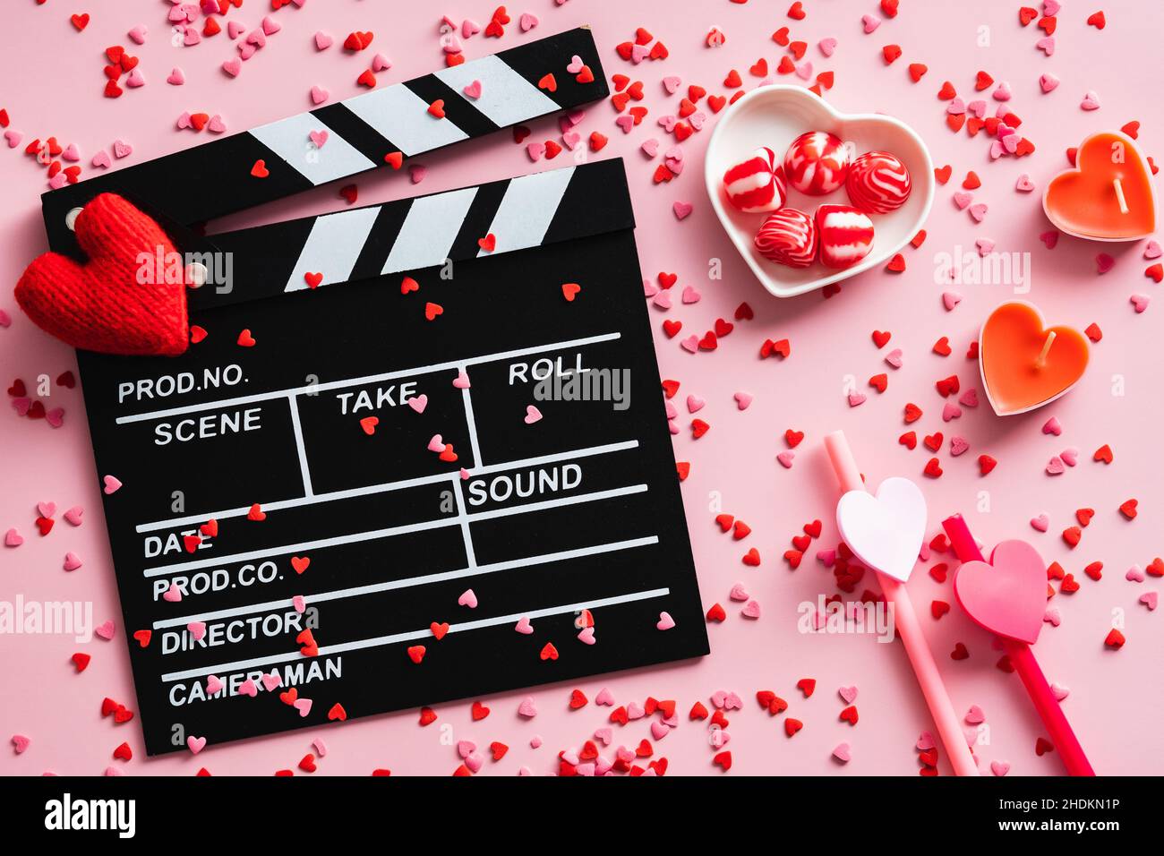 Romantisches Filmkonzept. Alles gute zum Valentinstag. Klappbrett, Herzen, Süßigkeiten, Konfetti auf rosafarbenem Tisch. Flach liegend, Draufsicht. Stockfoto