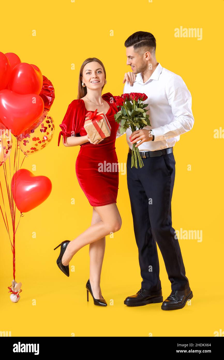Glückliches junges Paar mit Geschenk und Blumen auf farbigem Hintergrund.  Valentinstag-Feier Stockfotografie - Alamy
