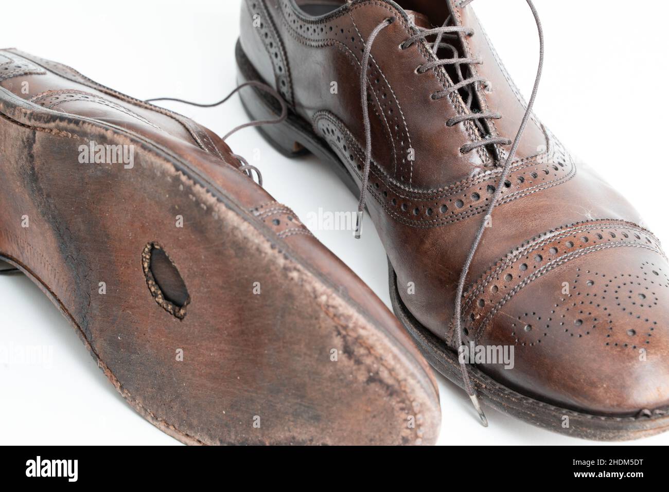 Studioaufnahme von alten, müden und kleinen zerkratzten Schnürsenkeln aus oxford-Schuhen in brünierter brauner Farbe auf weißem Hintergrund. Loch in der Sohle des Stockfoto