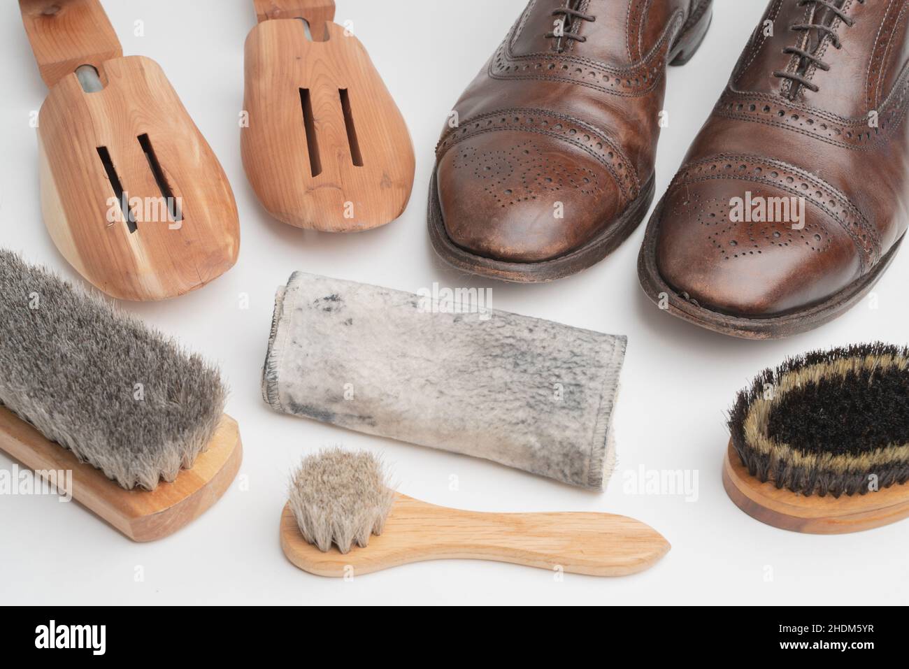 Studioaufnahme von alten, müden und kleinen zerkratzten Schnürsenkeln aus oxford-Schuhen in brünierter brauner Farbe auf weißem Hintergrund. Drei Bürsten von verschiedenen Stockfoto