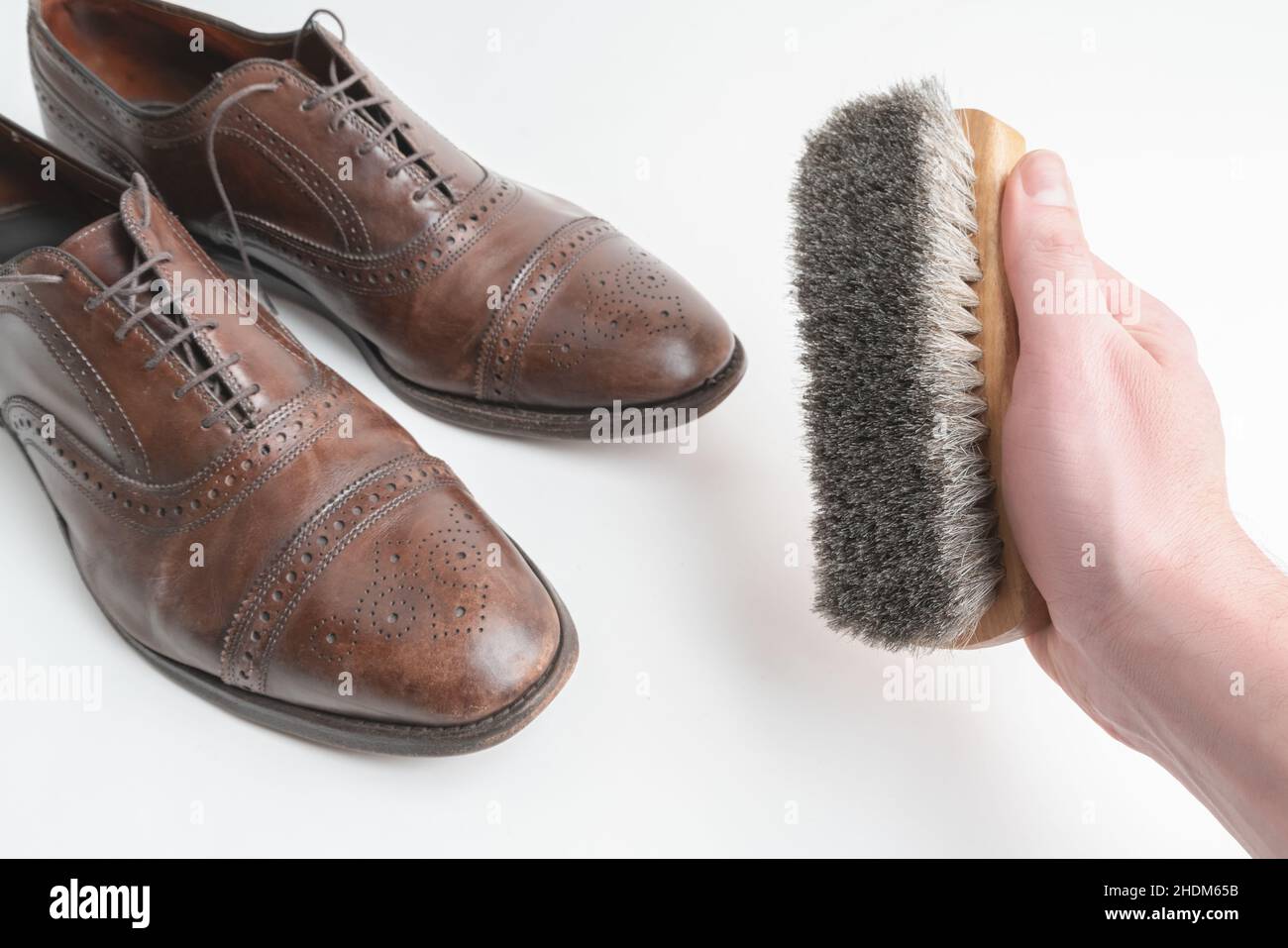 Studioaufnahme von alten, müden und kleinen zerkratzten Schnürsenkeln aus oxford-Schuhen in brünierter brauner Farbe auf weißem Hintergrund. Rechte männliche Hand, die A hält Stockfoto