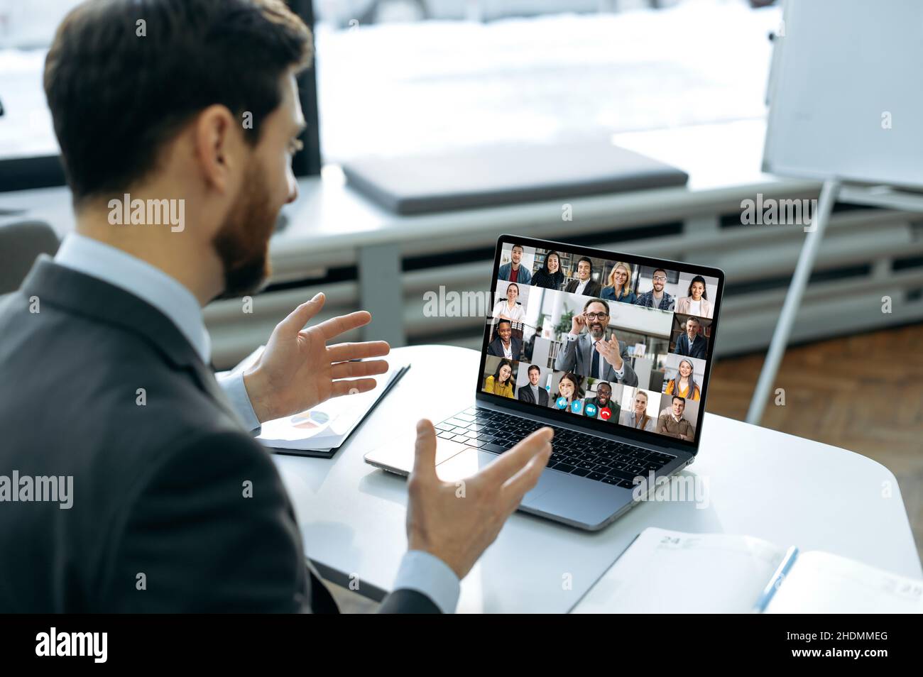 Remote-Geschäftstreffen. Erfolgreicher Mann mit einem Laptop, der bei einem Videoanruf mit Geschäftskollegen spricht. Eine Gruppe verschiedener, multirassischer Geschäftsleute auf dem Laptop-Bildschirm, die eine Videokonferenz abhalten Stockfoto