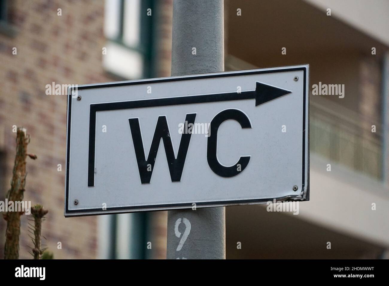 Nahaufnahme des weißen WC-Schildes mit schwarzen Buchstaben und Pfeil nach rechts auf der Säule Stockfoto