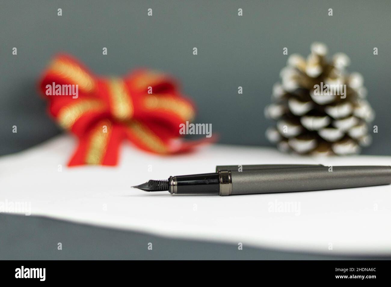 Makro eines Stifts, der auf einem weißen Stück Papier mit einem verschwommenen Hintergrund aus rotem Bogen und Eichel liegt Stockfoto