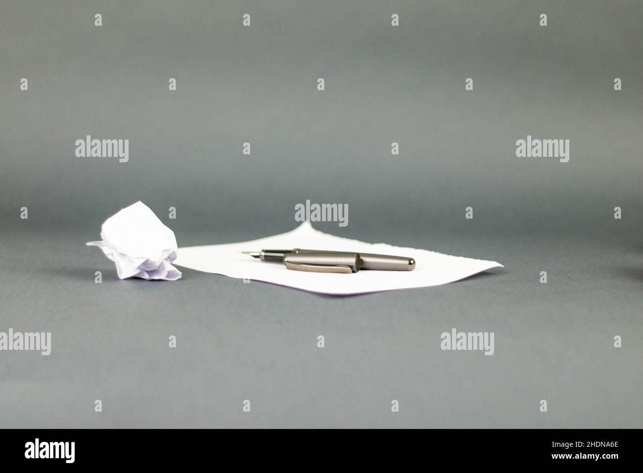 Nahaufnahme eines faltigen Papiers neben einem Stift, der auf einem Buchstaben mit grauem Hintergrund liegt Stockfoto
