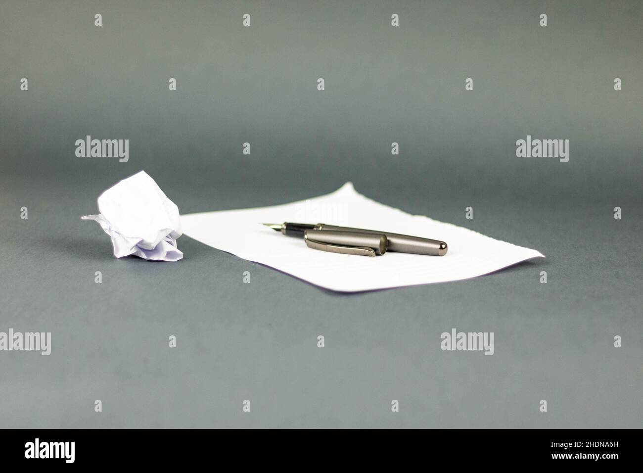 Nahaufnahme eines faltigen Papiers neben einem Stift, der auf einem Buchstaben mit grauem Hintergrund liegt Stockfoto