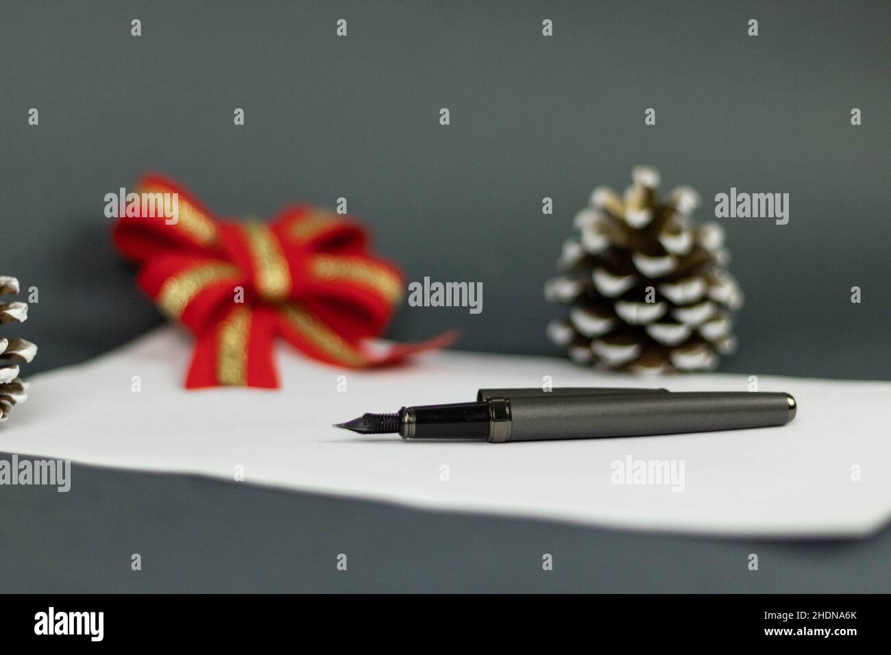 Nahansicht eines Stifts, der auf einem weißen Blatt Papier mit einem verschwommenen Hintergrund aus rotem Bogen und Eichel liegt Stockfoto
