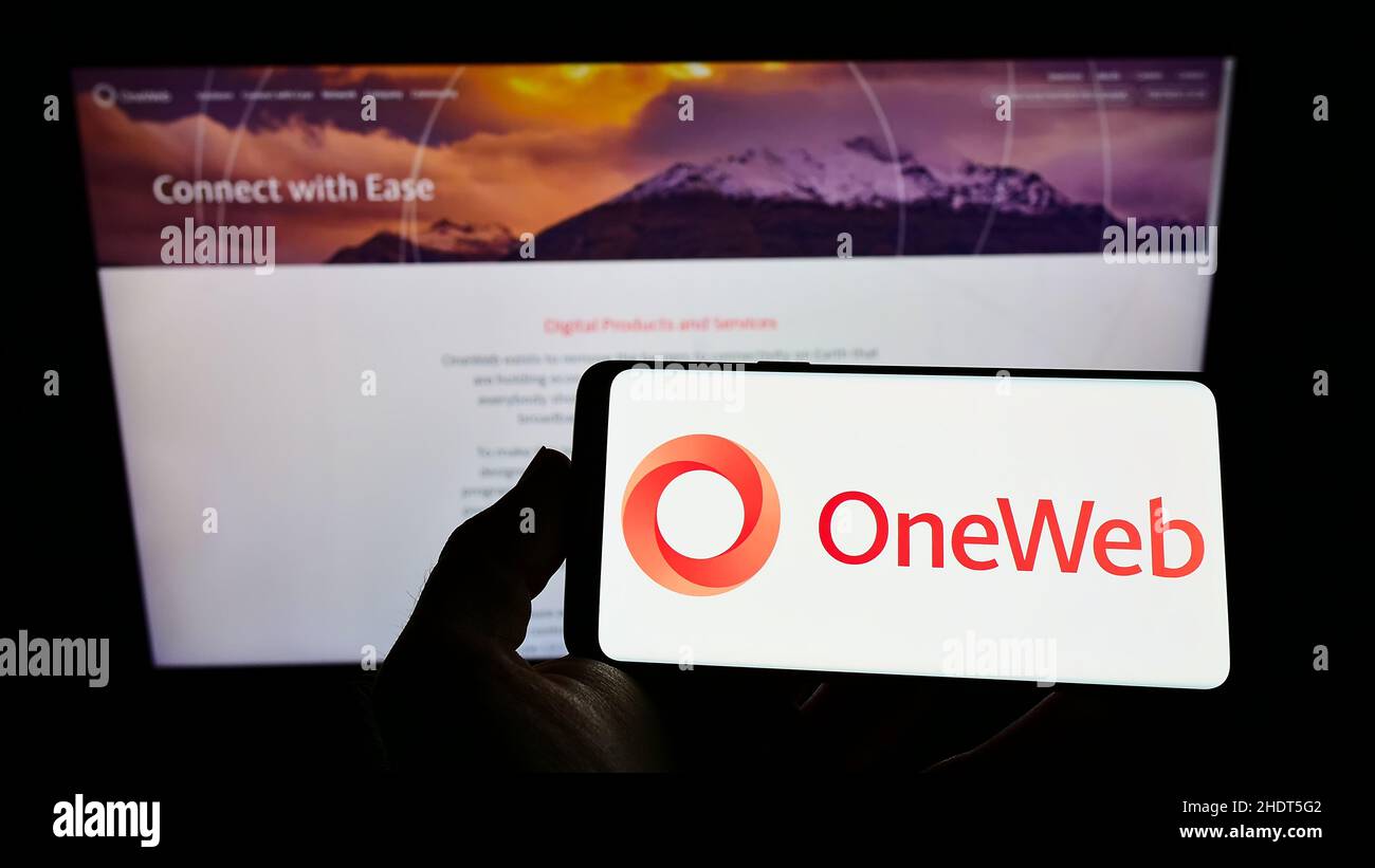 Person, die das Smartphone mit dem Logo der Firma Network Access Associates Ltd. (OneWeb) auf dem Bildschirm vor der Website hält. Konzentrieren Sie sich auf die Telefonanzeige. Stockfoto
