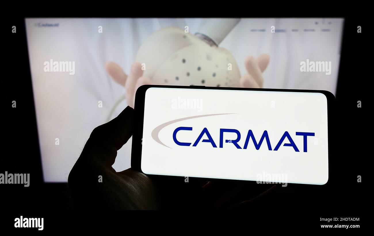 Person, die Mobiltelefon mit dem Logo des französischen Medizintechnik-Unternehmens Carmat SA auf dem Bildschirm vor der Business-Webseite hält. Konzentrieren Sie sich auf die Telefonanzeige. Stockfoto