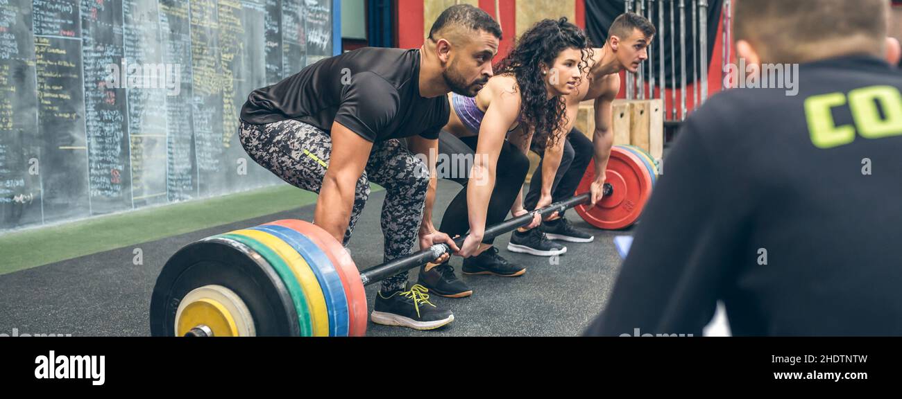 Gemischtes Team, das mit dem Trainer Gewichte im Fitnessstudio hebt Stockfoto