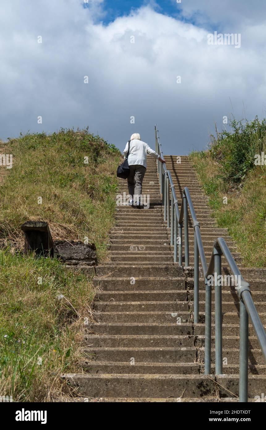 Eine Frau, die eine schwere Kameratasche trägt und eine steile Treppe hinaufsteigt, ist fit für die ältere Frau, Sywell Country Park, Northamptonshire, Großbritannien Stockfoto