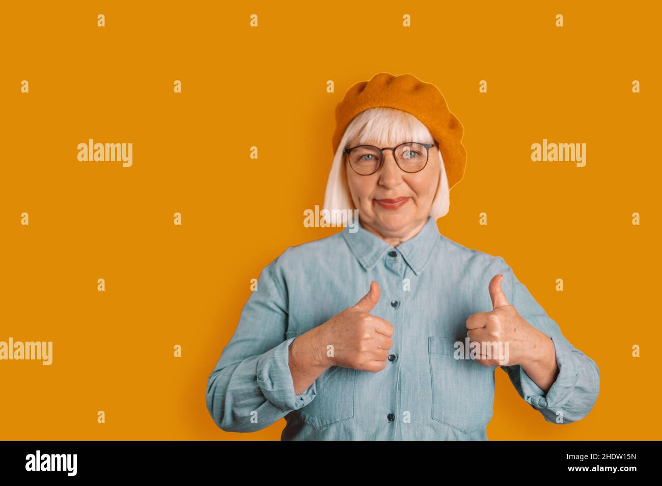Porträt der kaukasischen 50s Frau zeigt Daumen nach oben gute Laune im Studio isoliert über hellen orangen Hintergrund Stockfoto