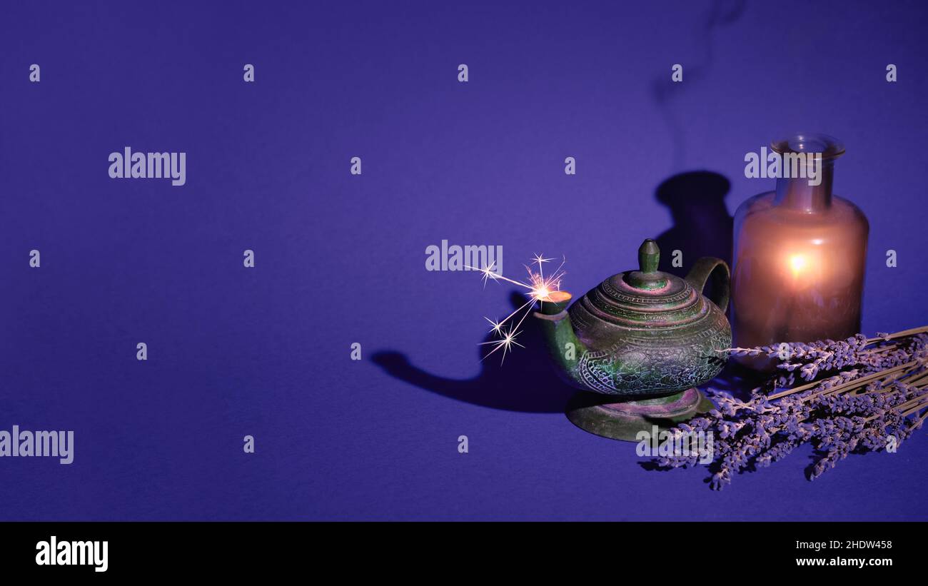 Magische orientalische Duftlampe mit Funkeln. Trockener Lavendel und leuchtendes Licht in Glasflasche auf dunkelviolettem Hintergrund. Weihrauch zur Meditation Stockfoto