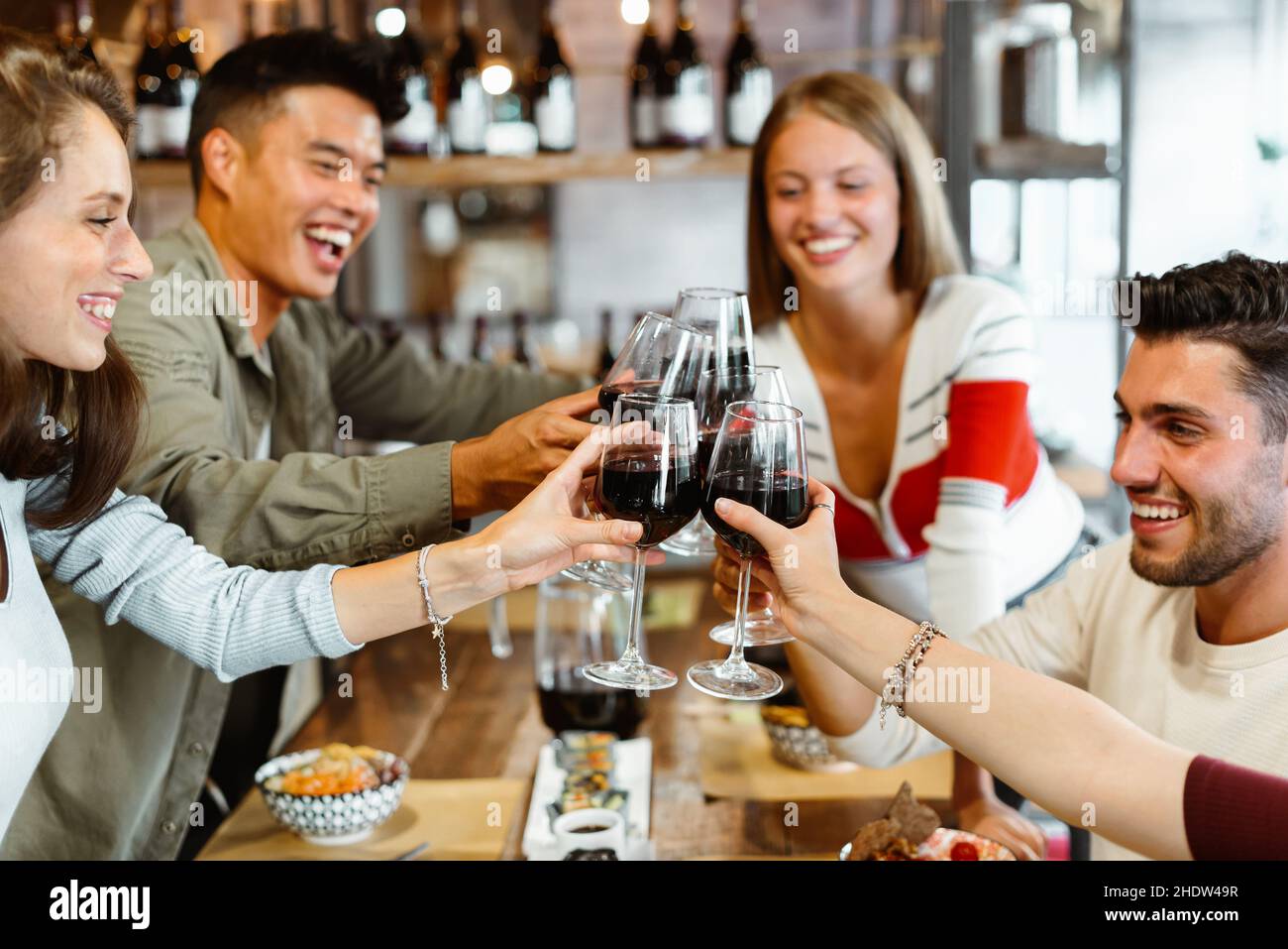 Eine bunte Gruppe multikultureller Freunde feiert im Restaurant gemeinsam lachend und scherzend, während sie sich mit einem Glas Rotwein anstoßen Stockfoto