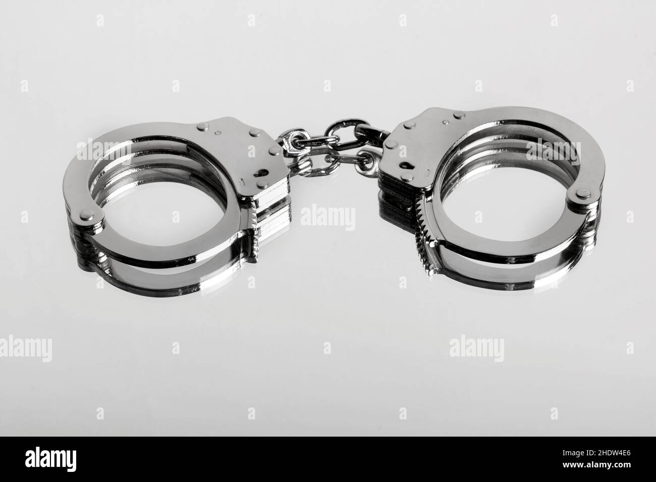 Studio-Nahaufnahme eines verschlossenen Paares von hiatt-Handschellen, die auf einer glänzenden Oberfläche als Symbol für Inhaftierung und Kriminalität gespiegelt sind Stockfoto