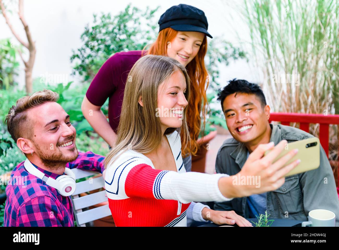 Eine multikulturelle Gruppe glücklicher junger Freunde, die zusammen auf einem Mobiltelefon ein Selfie machen, lachen und lächeln, während sie als Gruppe im Freien posieren Stockfoto