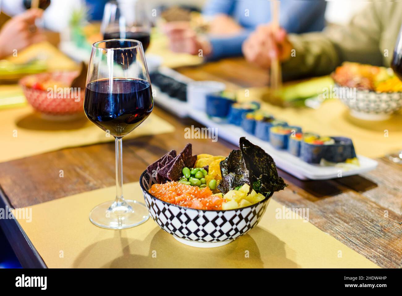 Eine Schüssel mit frischem Poke und einem Glas Rotwein, serviert auf einem Restauranttisch, mit verschiedenen Meeresfrüchten und Sushi, die für eine Gruppe von Leuten zum Essen bereit sind Stockfoto