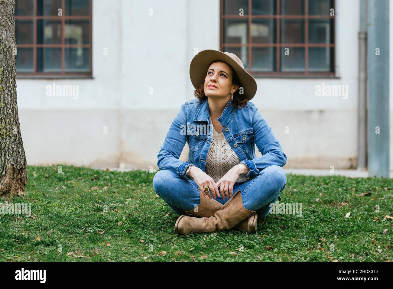 Frau lächelt, während sie sich auf dem Gras auf der Straße der Stadt entspannt. Stockfoto