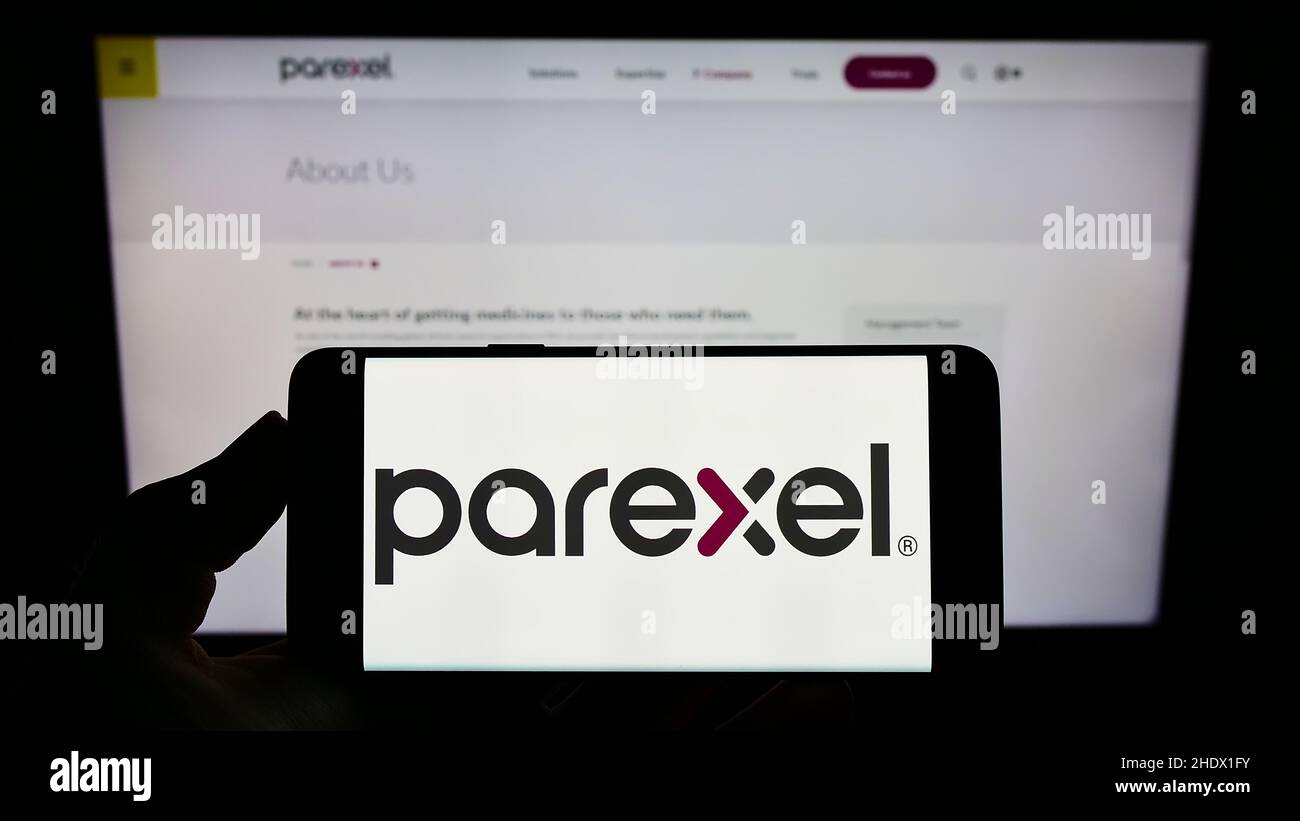 Person, die das Mobiltelefon mit dem Logo des amerikanischen Unternehmens Parexel International Corporation auf dem Bildschirm vor der Webseite hält. Konzentrieren Sie sich auf die Telefonanzeige. Stockfoto