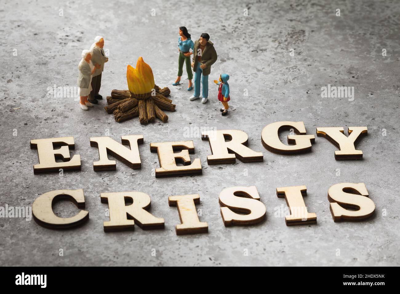 Spielzeugmänner aus Kunststoff sonnen sich am Feuer, Worte aus Holzbuchstaben auf dem Tisch, ein Konzept zum Thema Energiekrise Stockfoto
