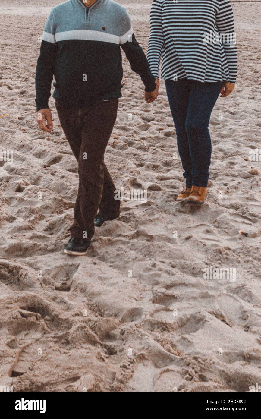 Niedliches Paar mit gestreifter Bluse, die die Hände auf einem sandigen Land hält Stockfoto