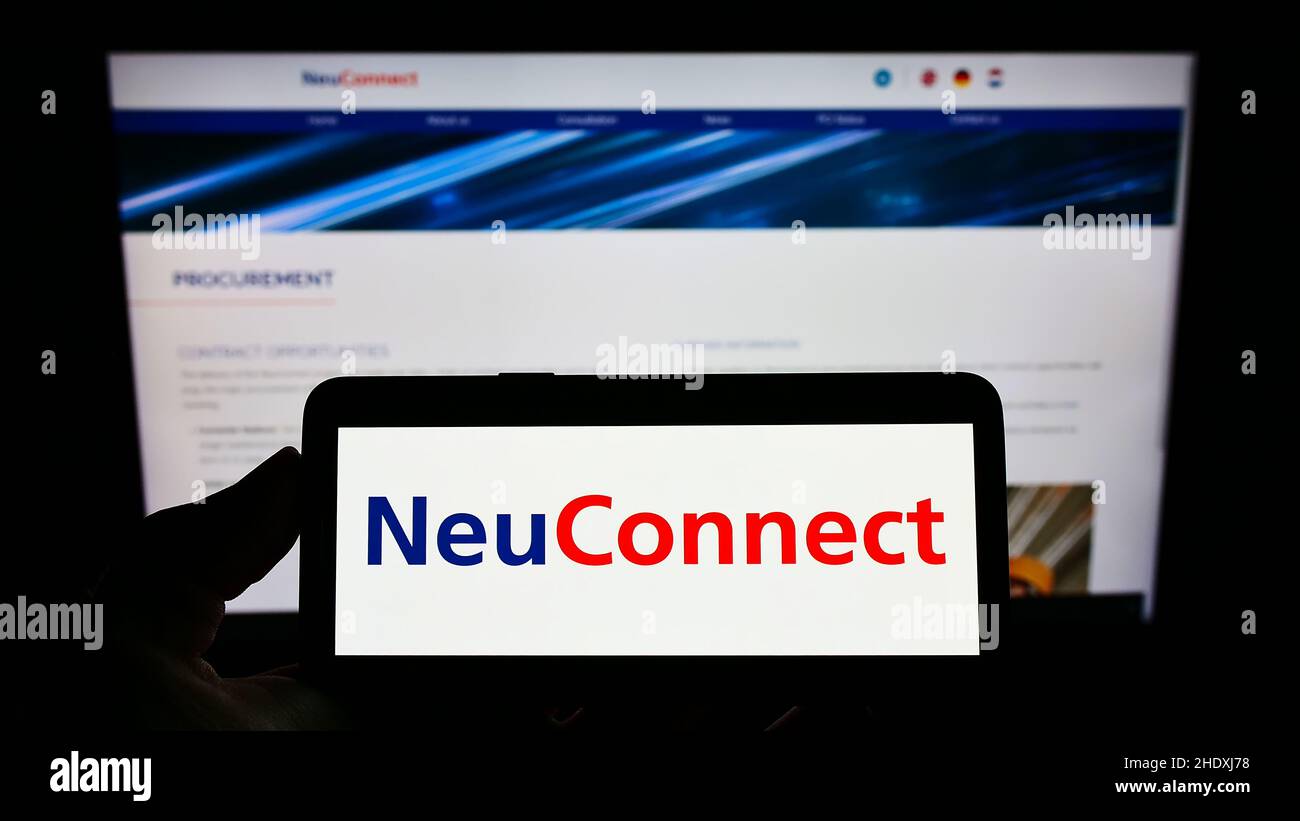 Person, die Mobiltelefon mit Logo des Kraftübertragungsprojekts NeuConnect Interconnector auf dem Bildschirm mit Webseite hält. Konzentrieren Sie sich auf die Telefonanzeige. Stockfoto