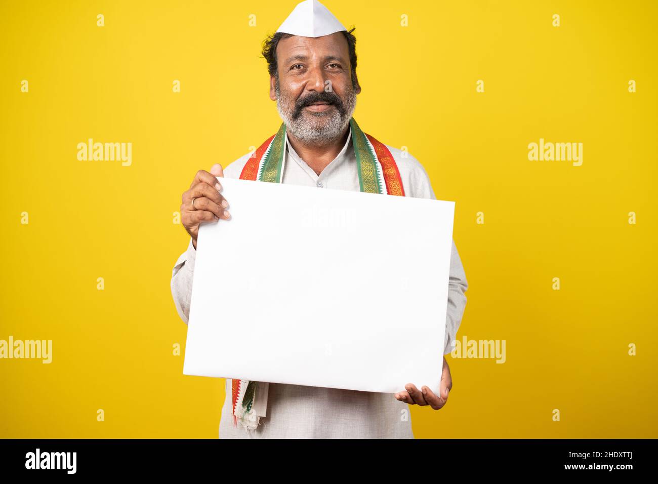 Porträt eines glücklichen lächelnden indischen Poliikers, der leere weiße Schildertafel hält, indem er die Kamera auf gelbem Studiohintergrund anschaut. Stockfoto