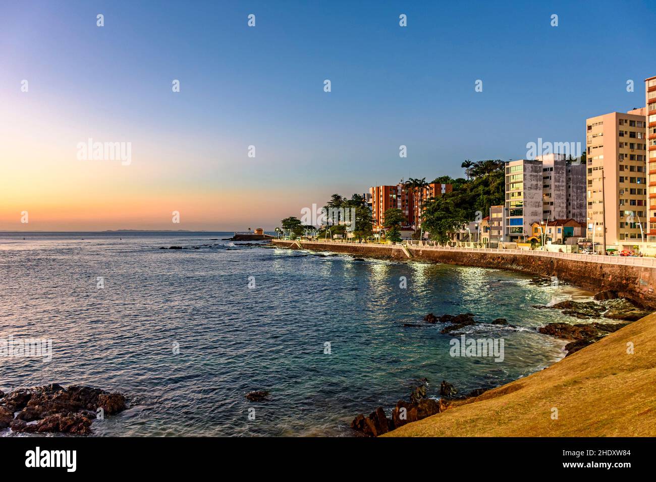 Strandpromenade in der touristischen Region der Stadt Salvador in Bahia während des Sonnenuntergangs mit dem Meer, Gebäuden, Straßen und Gehwegen Stockfoto