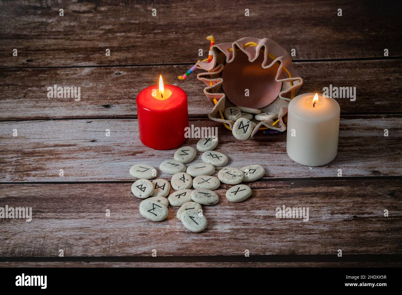 runensteine mit schwarzen Symbolen für Wahrsagerei mit Kerzen auf einem Holztisch Stockfoto