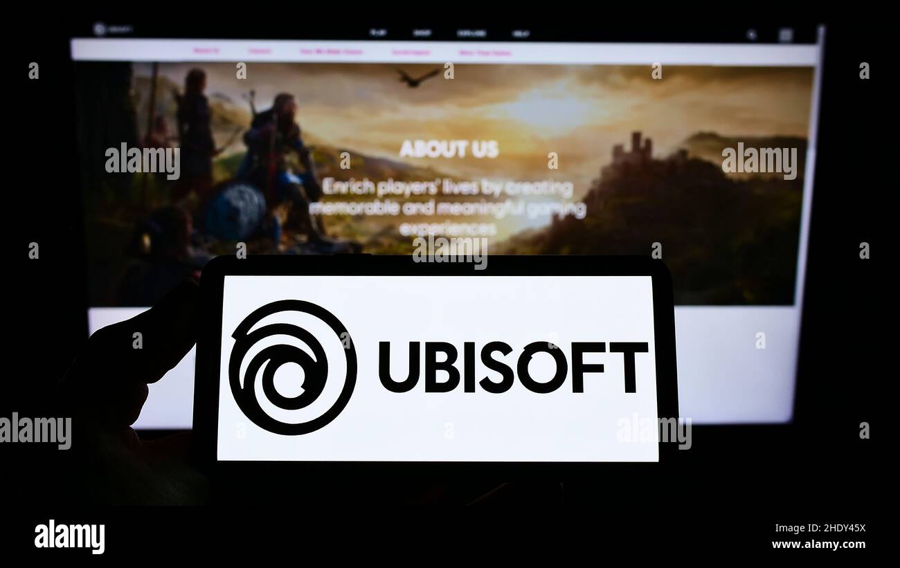 Person, die das Smartphone mit dem Logo des französischen Videospielunternehmens Ubisoft Entertainment SA auf dem Bildschirm vor der Website hält. Konzentrieren Sie sich auf die Telefonanzeige. Stockfoto