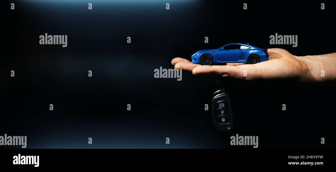 Hand halten Miniatur-Automobil-Modell und Schlüssel auf dunklem Hintergrund. Auto kaufen und mieten. Banner Stockfoto