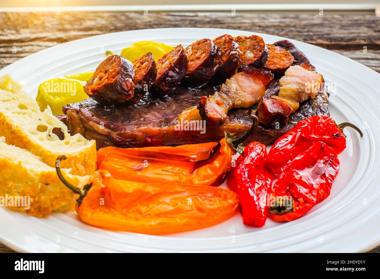 Club Steak mit gegrillten Würstchen und Paprika auf weißem Teller mit Sonnenlicht Stockfoto