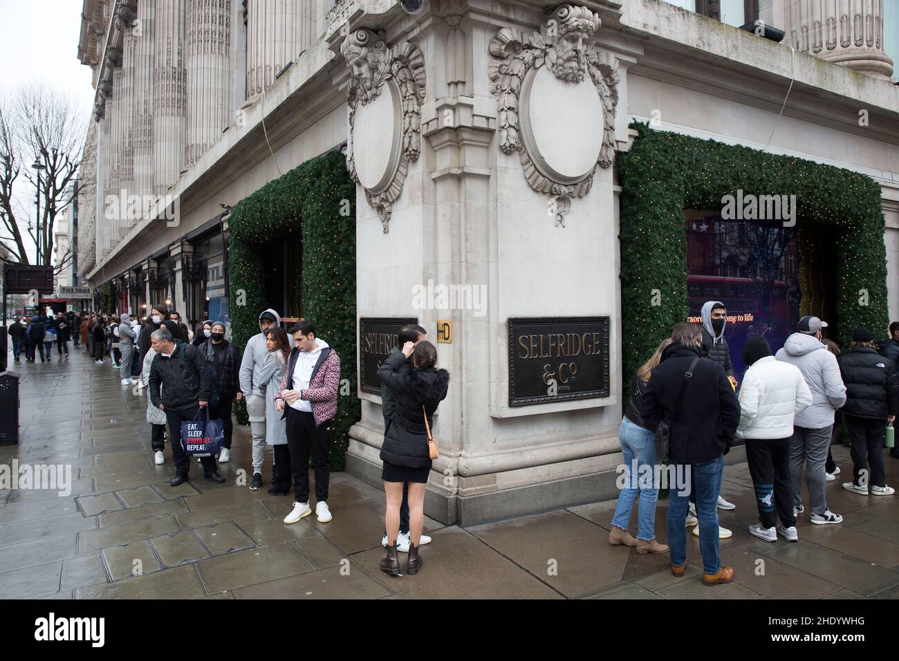 Vor der Eröffnung am zweiten Weihnachtsfeiertag stehen Menschen vor dem Kaufhaus Selfridges an, trotz der nassen Witterungsverhältnisse auf der Oxford Street in London. Stockfoto