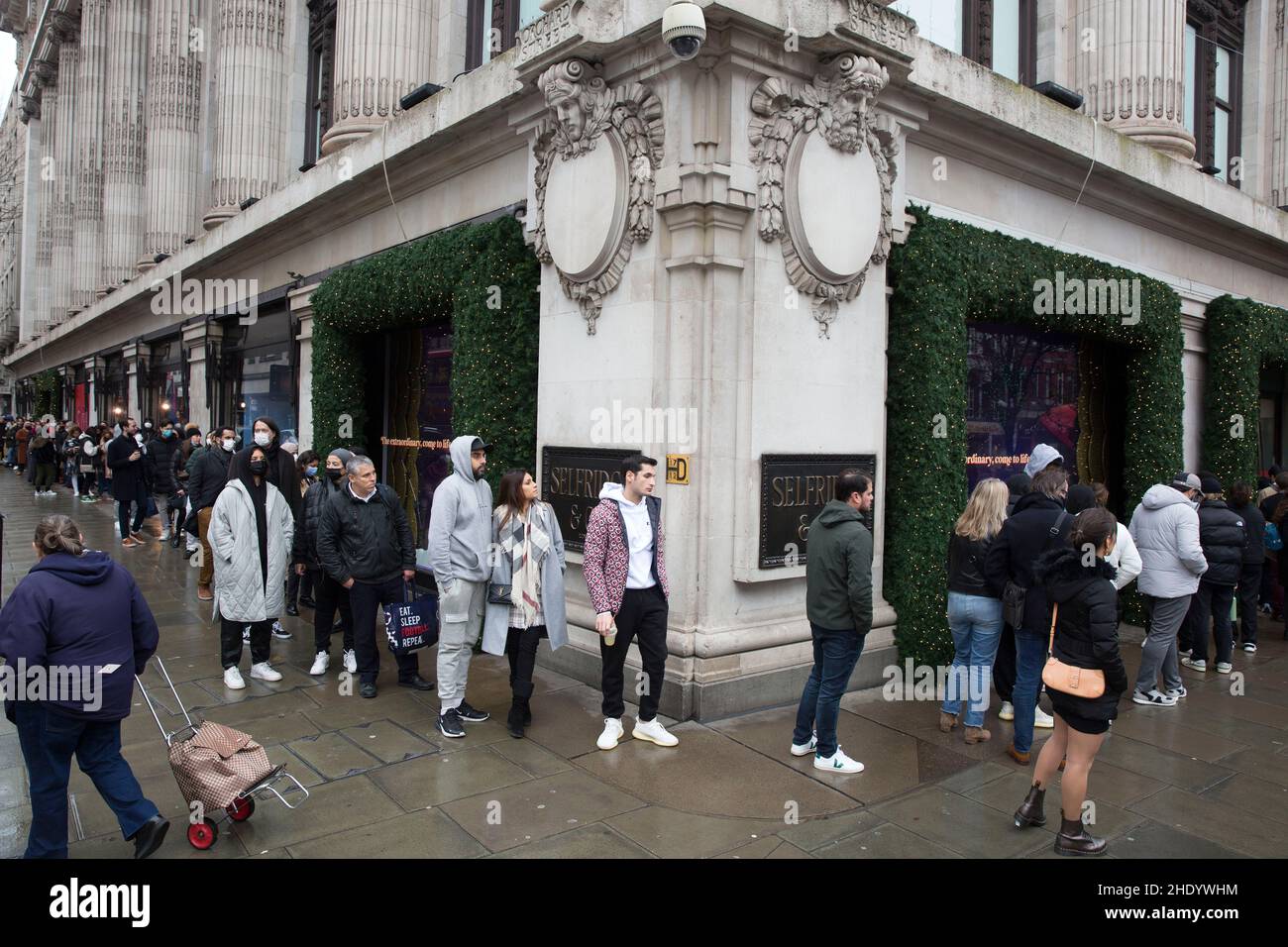 Vor der Eröffnung am zweiten Weihnachtsfeiertag stehen Menschen vor dem Kaufhaus Selfridges an, trotz der nassen Witterungsverhältnisse auf der Oxford Street in London. Stockfoto