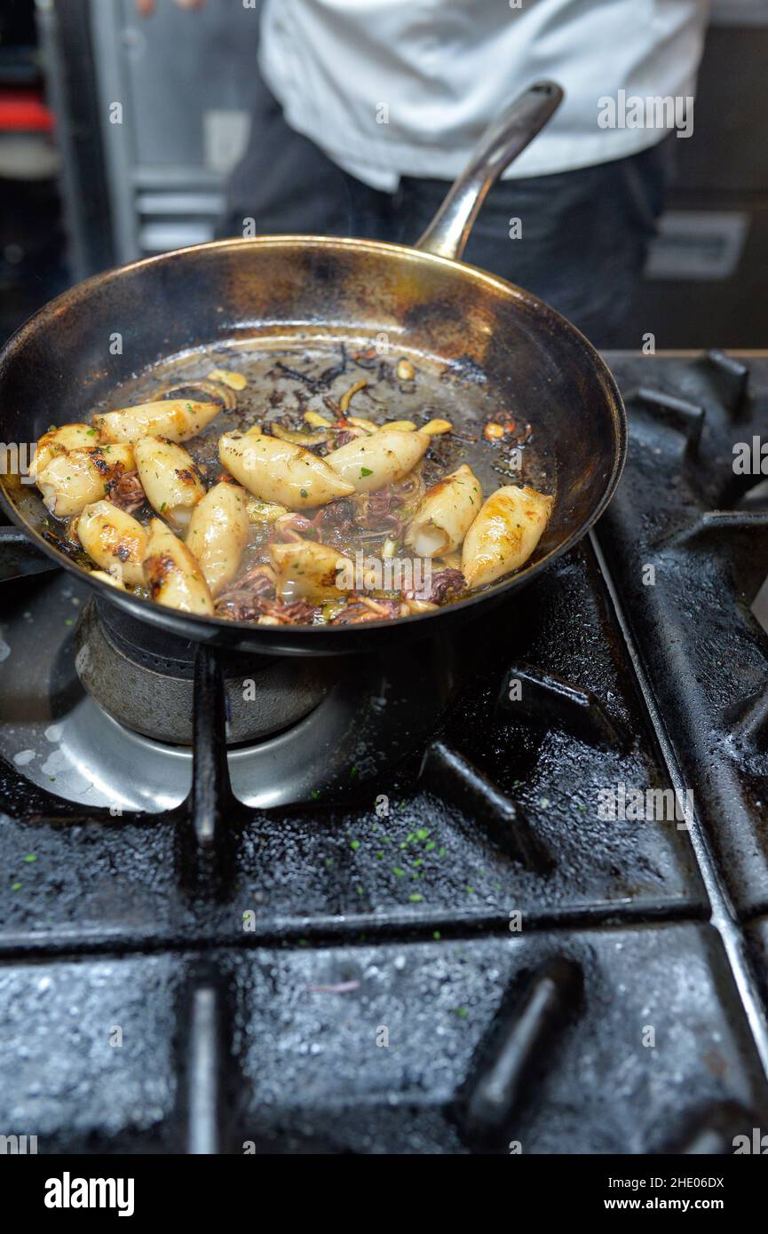 In einer Restaurantküche werden Calamari vom Küchenchef auf einem Gasherd gegrillt. Stockfoto