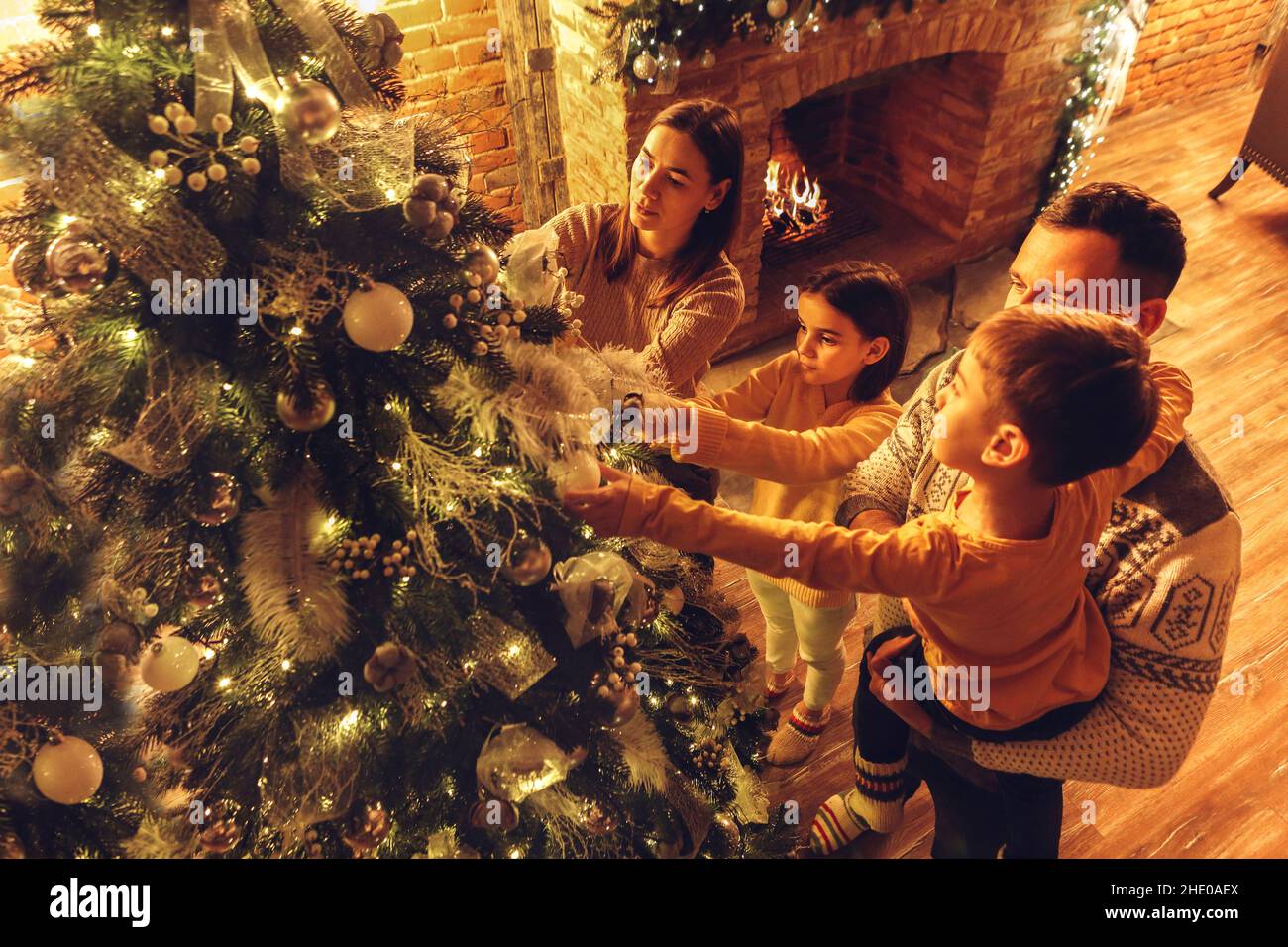 Junge glückliche europäische Familie mit zwei Kindern, die das Haus für die Neujahrsfeier vorbereiten. Eltern mit kleinen Kindern dekorieren Weihnachtsbaum, hängen xm Stockfoto