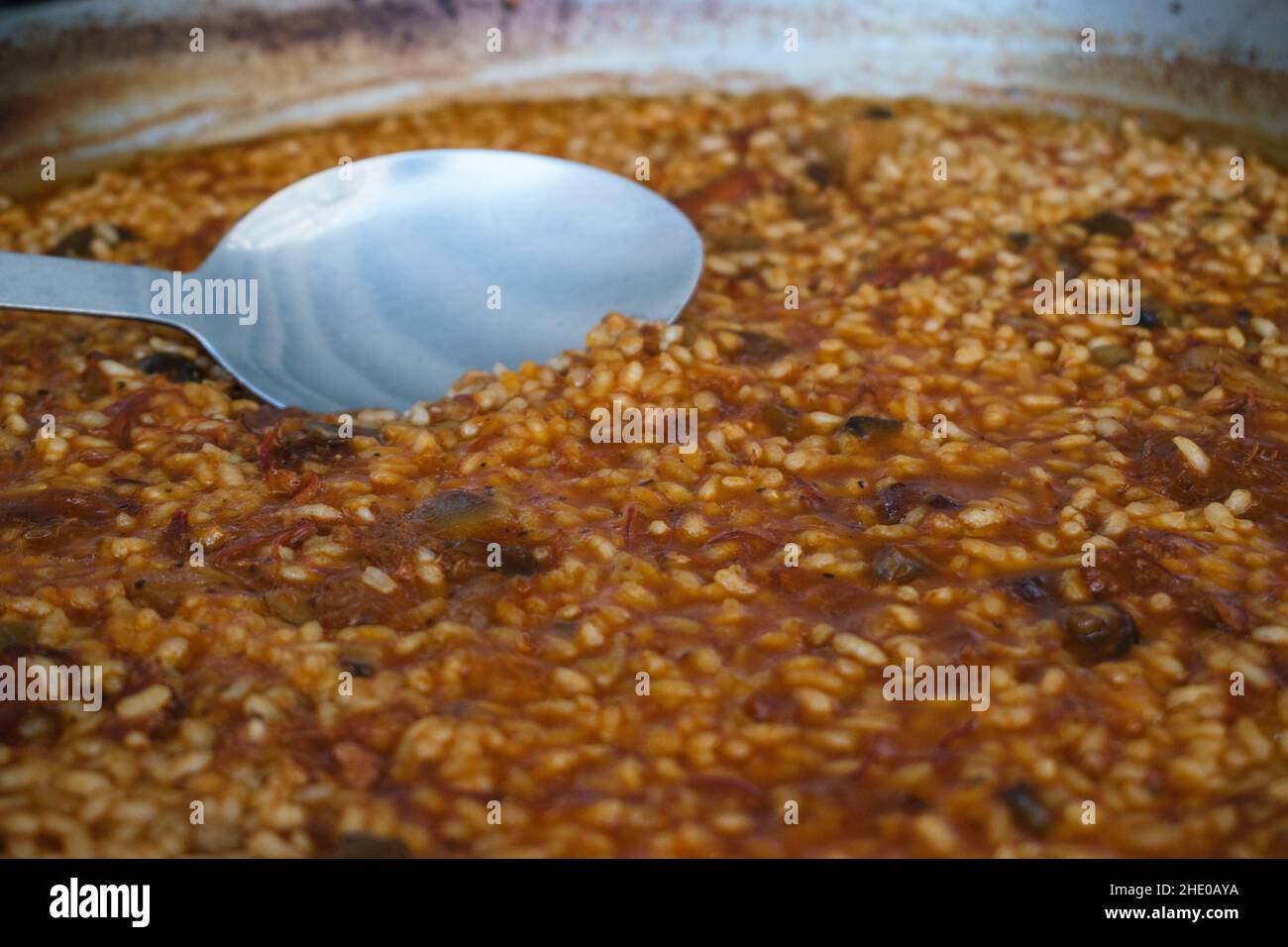 Nahaufnahme einer Paella aus Ente und Pilzreis mit einem Löffel in der Mitte Stockfoto