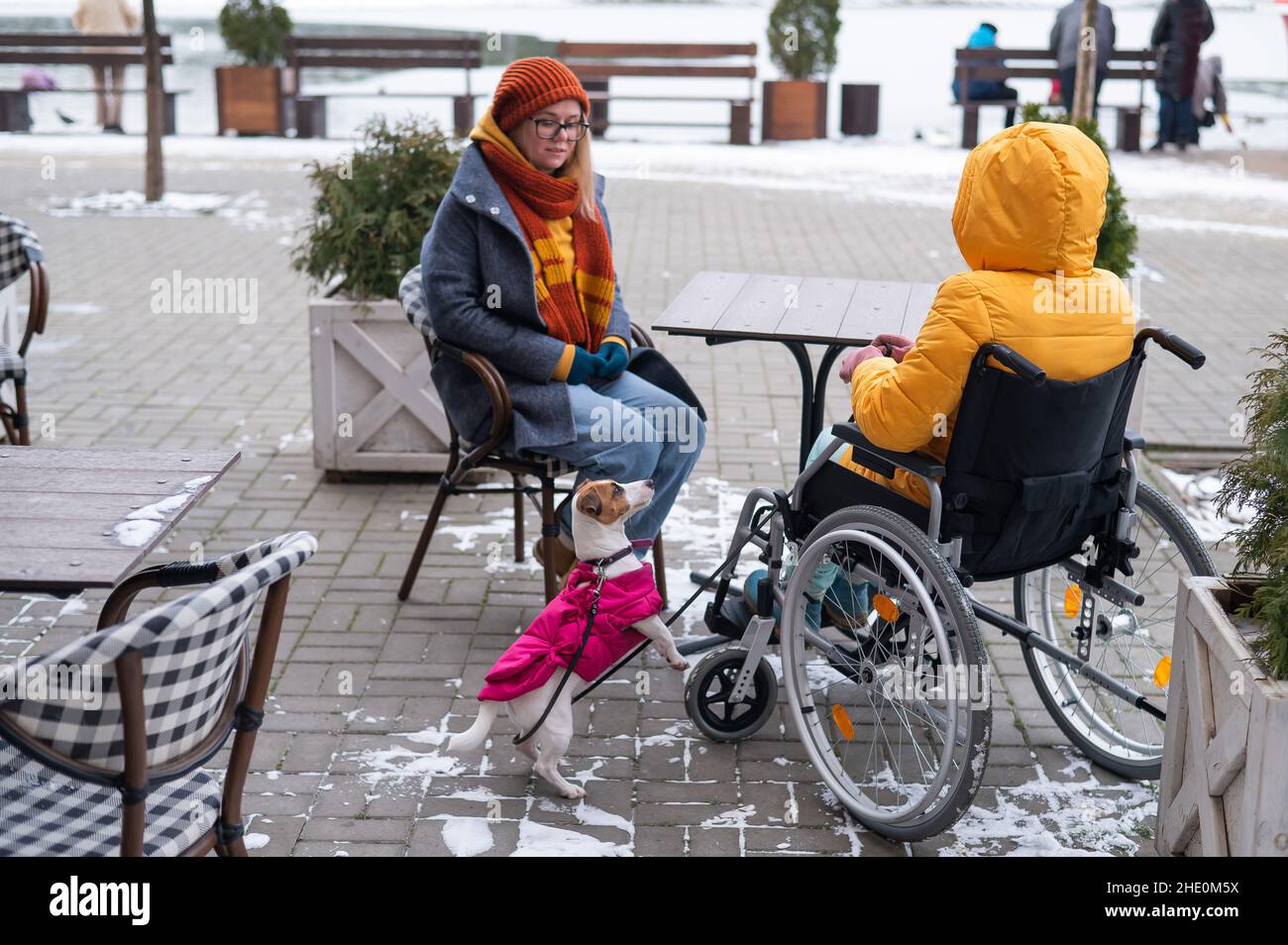 Zwei Freundinnen im Winter in einem Café auf einer Straßenterrasse. Frau im Rollstuhl. Stockfoto