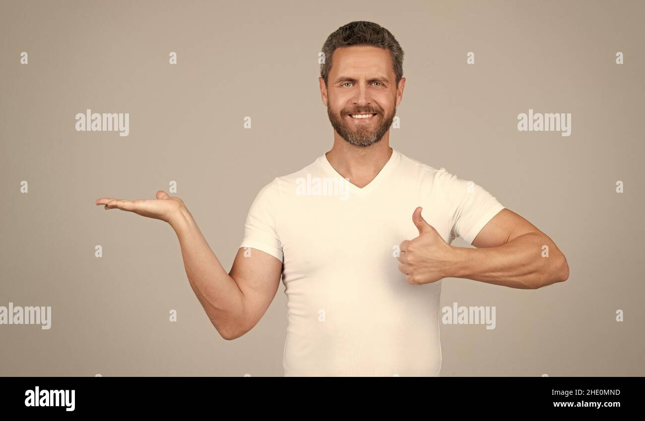 Das beste Produkt präsentieren. Glücklicher Mann zeigt die offene Hand und zeigt den Daumen nach oben. Produktpräsentation Stockfoto