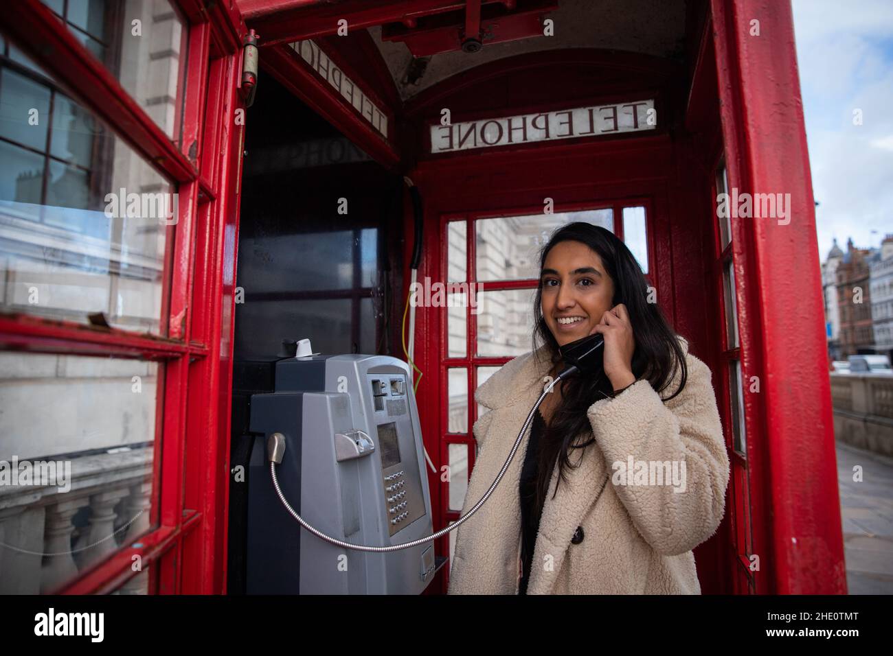 Mädchen telefoniert in einer roten Telefonbox in London. Schöne lächelnde und attraktive Frau am Telefon Stockfoto