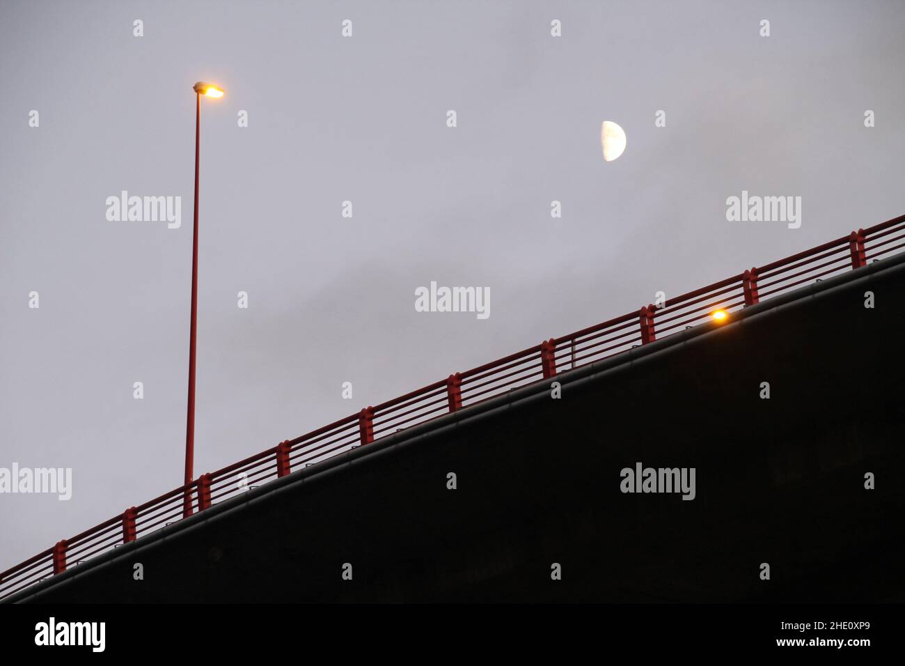Eine Straßenbrücke mit einer Straßenbeleuchtung am Abend unter einem bewölkten Himmel Stockfoto
