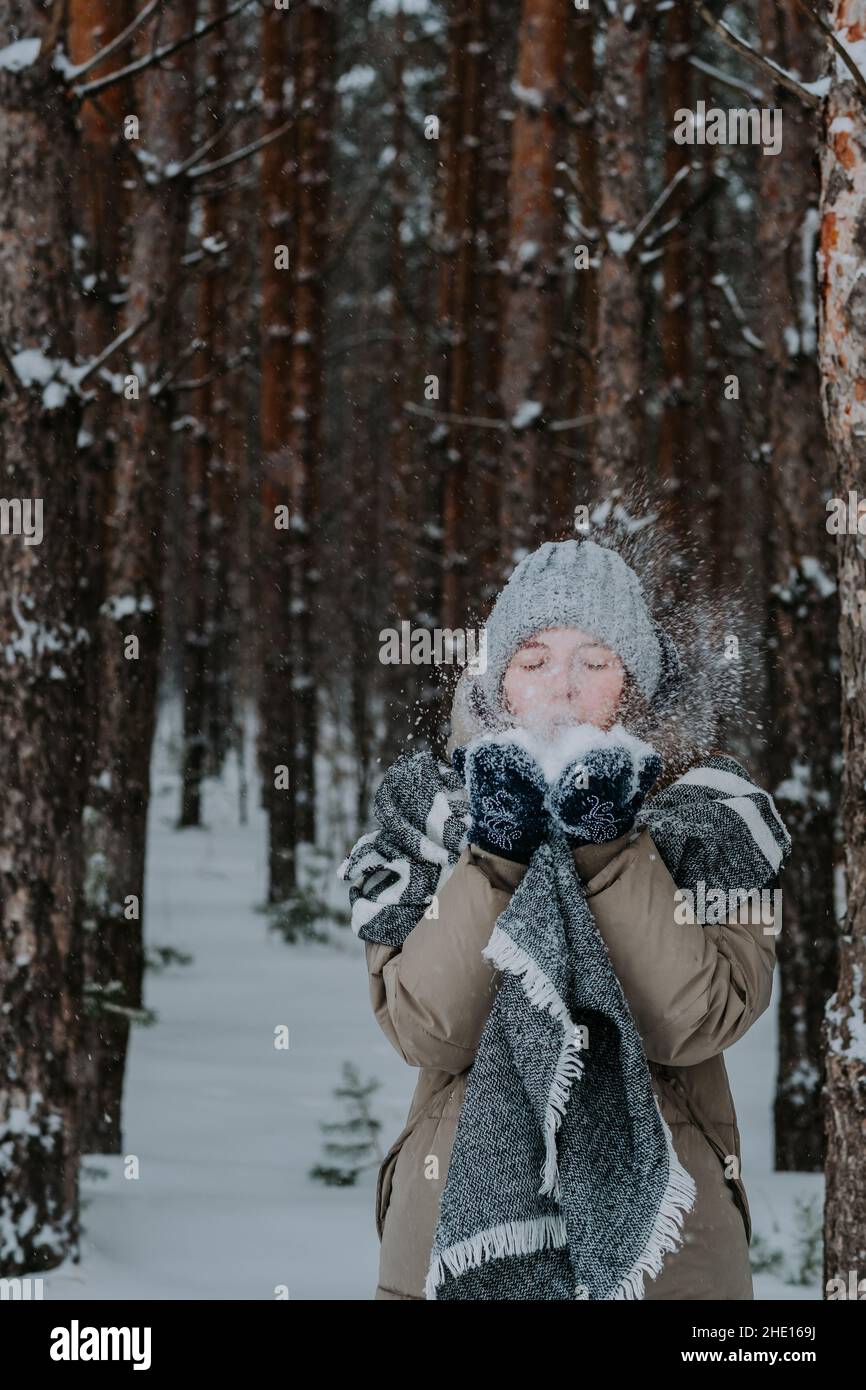 Mädchen bläst Schnee von ihren Händen. Ein Mädchen in einem Hut wirft Schnee in den Winterwald. Frohe Winterferien. Liebe für den Winter. Winter im Norden. Stockfoto