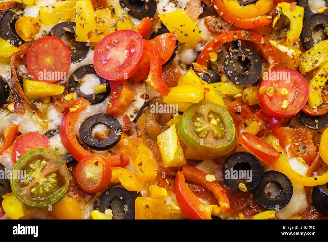 Detail der Beläge auf einer hausgemachten Pizza mit Oliven, Tomaten, Paprika, Pepperoni, Kräutern, Tomatensauce und Käse Stockfoto