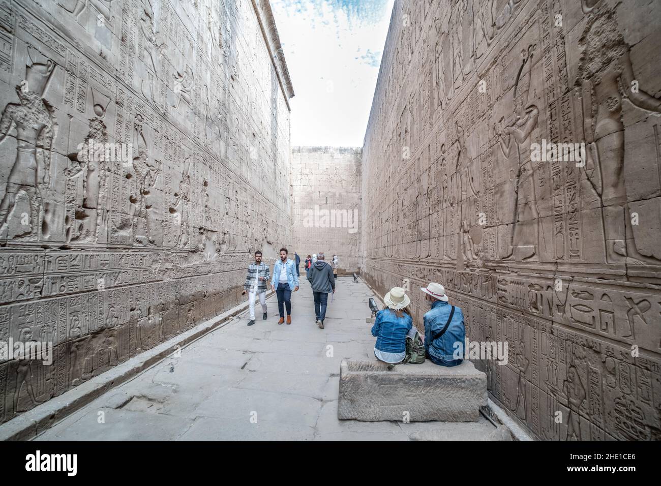 Ein reich eingeschriebener und geschnitzter Durchgang um den Edfu-Tempel, wo die Steinmauern dicht mit Hieroglyphen und Reliefskulpturen bedeckt sind. Stockfoto