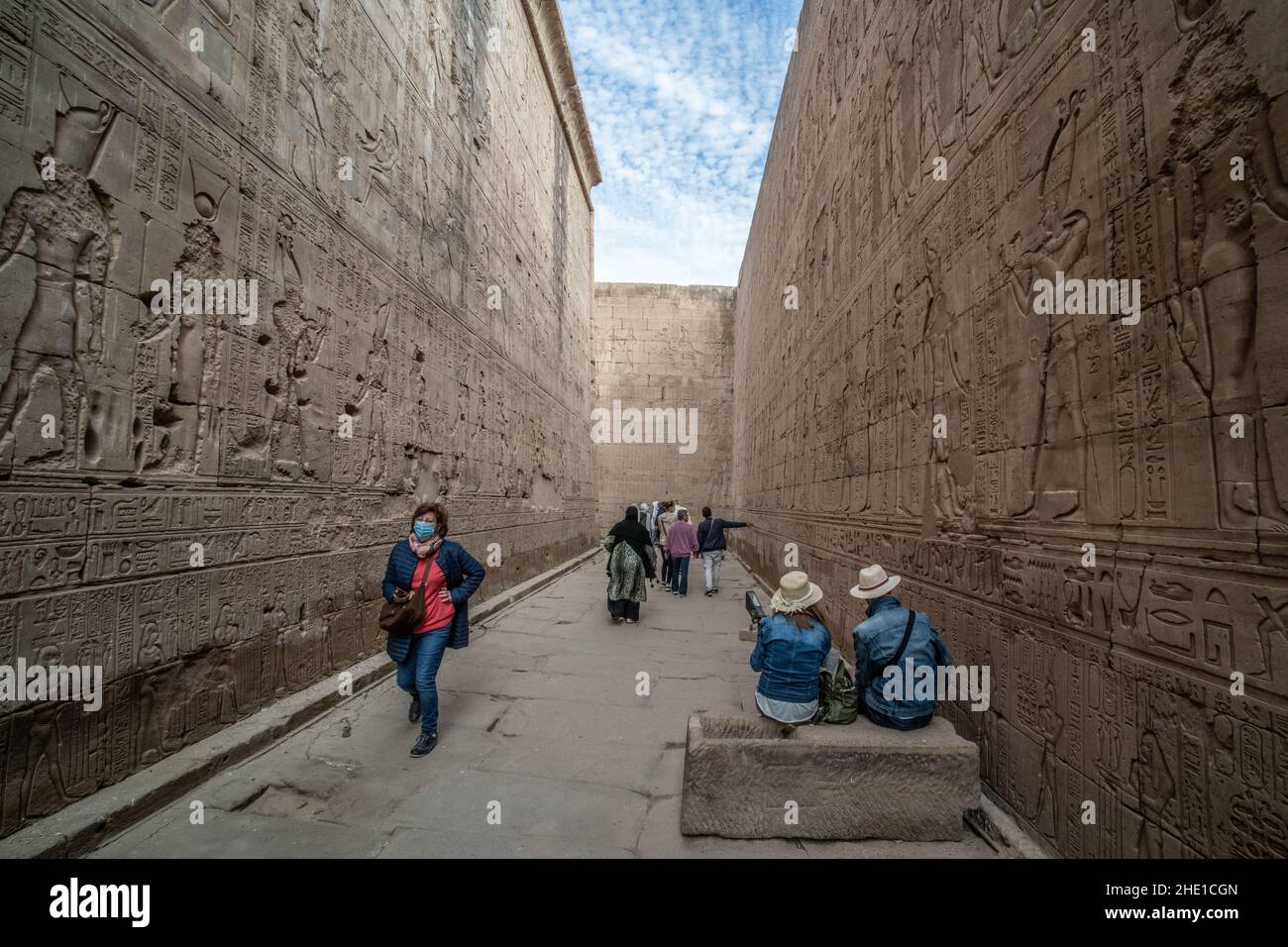 Ein reich eingeschriebener und geschnitzter Durchgang um den Edfu-Tempel, wo die Steinmauern dicht mit Hieroglyphen und Reliefskulpturen bedeckt sind. Stockfoto
